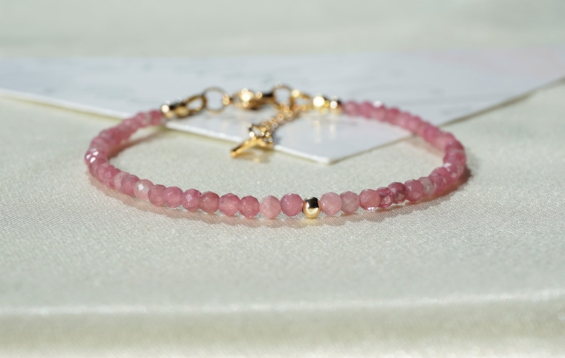 Op de afbeelding: Een delicate armband van roze edelstenen met een gouden sluiting en een enkele gouden kraal. De armband is gemaakt van kleine, ronde kralen en is perfect voor dagelijks gebruik.