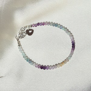 May include: A delicate bracelet with a silver heart charm and a gradient of pastel blue, green, purple, and pink beads.