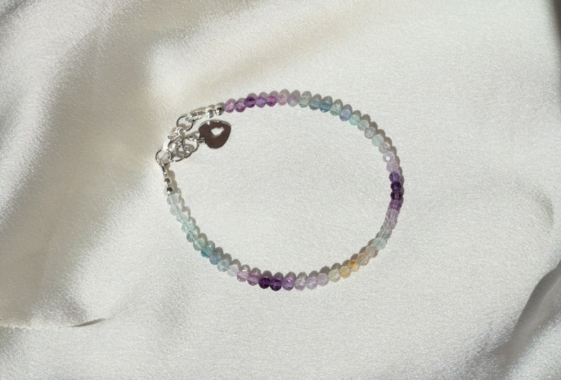 May include: A delicate bracelet with a silver heart charm and a gradient of pastel blue, green, purple, and pink beads.