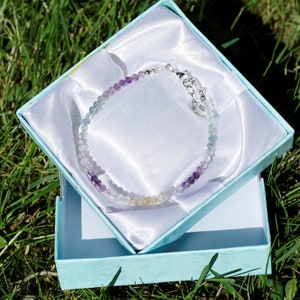 May include: A rainbow fluorite gemstone bracelet with a silver clasp, displayed in a light blue gift box.