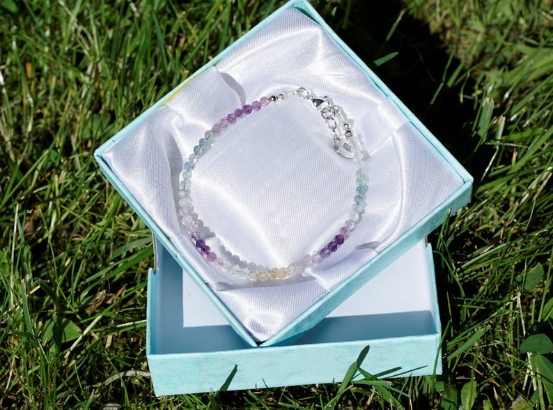 May include: A rainbow fluorite gemstone bracelet with a silver clasp, displayed in a light blue gift box.