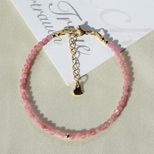 Op de afbeelding: Een delicate armband van roze edelstenen met een gouden hartbedel en een karabijn sluiting.