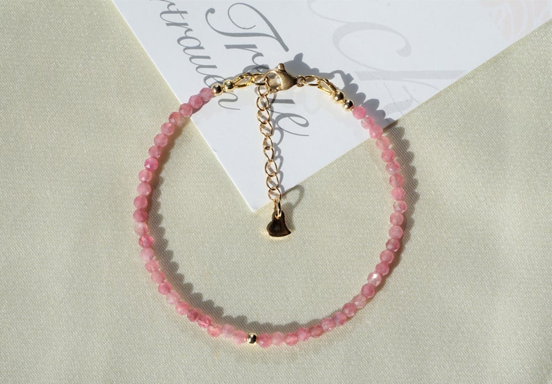 Op de afbeelding: Een delicate armband van roze edelstenen met een gouden hartbedel en een karabijn sluiting.