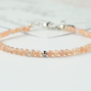 Op de afbeelding: Een delicate armband gemaakt met kleine, licht oranje sunstone kralen en een zilveren kraal accent.