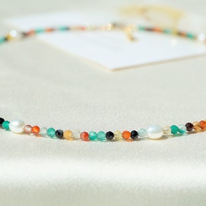 May include: A colorful beaded necklace with white pearls and a gold clasp. The necklace features a variety of colors, including green, orange, red, and black.
