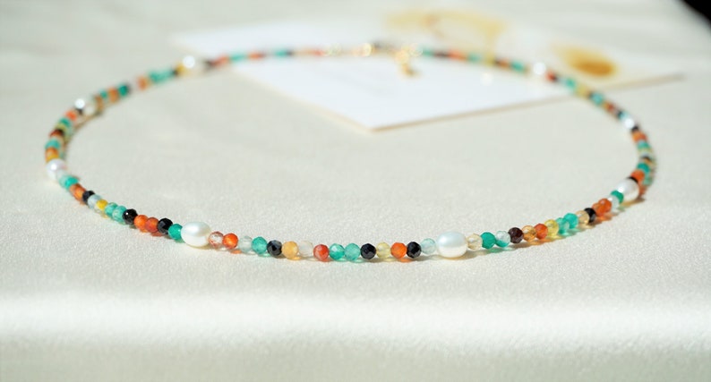 May include: A colorful beaded necklace with white pearls and a gold clasp. The necklace features a variety of colors, including green, orange, red, and black.