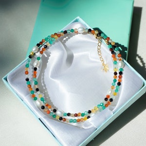 May include: A multi-strand necklace with green, orange, brown, black, and white beads in a turquoise gift box.