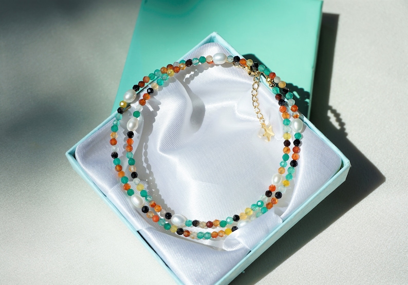May include: A multi-strand necklace with green, orange, brown, black, and white beads in a turquoise gift box.