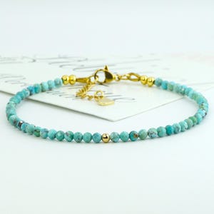Könnte beinhalten: Ein zartes Armband aus türkisfarbenen Edelsteinen mit goldenen Akzenten. Das Armband besteht aus kleinen, facettierten Türkisperlen und hat einen goldenen Verschluss und eine kleine goldene Perle.