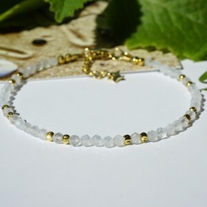 Op de afbeelding: Een delicate armband met kleine, gefacetteerde doorschijnende witte kralen afgewisseld met piepkleine, gepolijste goudkleurige metalen kralen. De armband bevat een goudkleurige metalen verlengketting met een kleine stervormige bedel.