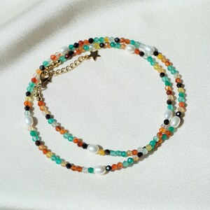May include: A multi-strand necklace with green, orange, black, and white beads. The necklace has a gold chain with a star charm.