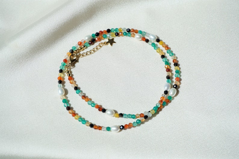 May include: A multi-strand necklace with green, orange, black, and white beads. The necklace has a gold chain with a star charm.