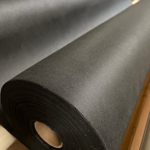 May include: A large roll of black landscape fabric, a type of weed barrier, is rolled up on a wooden frame.
