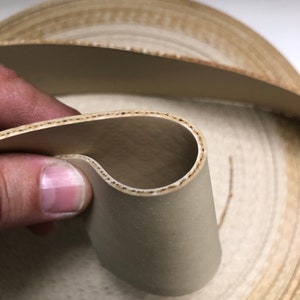 May include: Close-up of a beige fabric tape with a zig-zag edge. The tape is folded in half, revealing the inside of the tape.