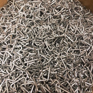 May include: A large pile of silver metal triangle shaped hooks.
