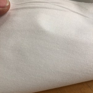 May include: White fabric with a smooth, silky texture. The fabric is folded in half, showing the inside of the fold.