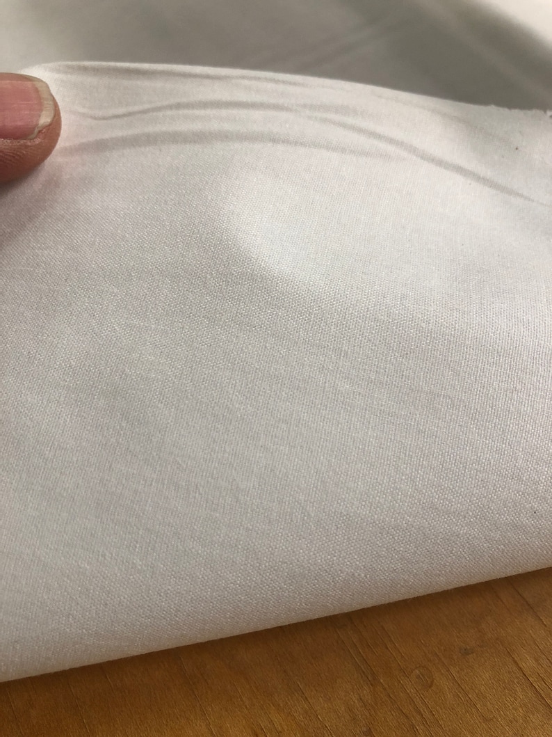 May include: White fabric with a smooth, silky texture. The fabric is folded in half, showing the inside of the fold.