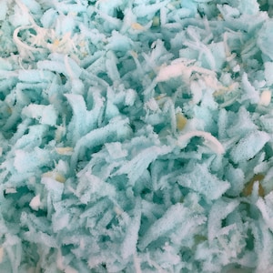 May include: A close-up of a bag filled with light blue shredded memory foam. The foam is soft and fluffy, and it looks like it would be comfortable to sleep on.