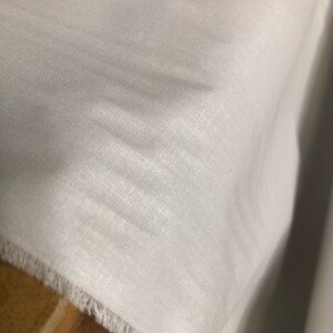 May include: White fabric with a slightly textured surface. The fabric has a raw edge.