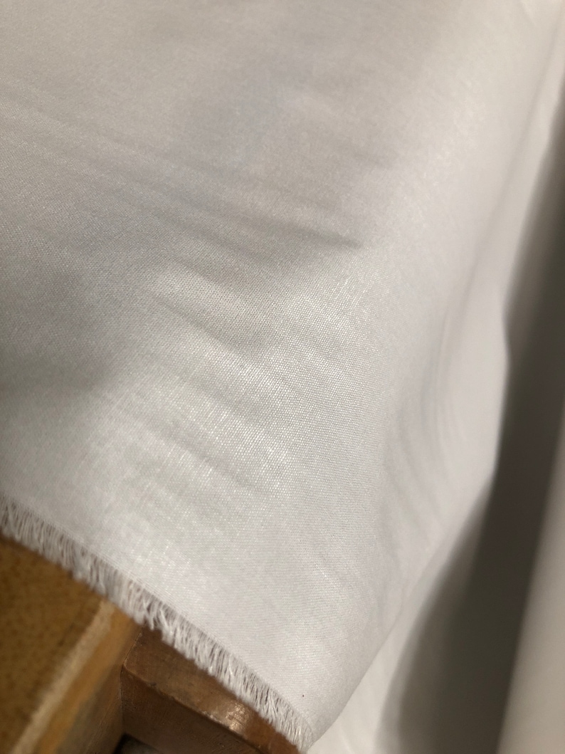 May include: White fabric with a slightly textured surface. The fabric has a raw edge.
