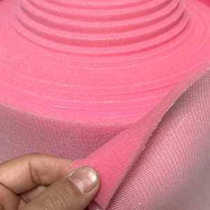 May include: A roll of pink hook and loop tape with a soft, fuzzy texture. The tape is folded over to show the hook side and the loop side.