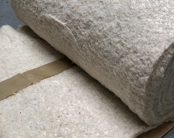 May include: A roll of white cotton batting, a natural fiber used for insulation and padding, is partially unrolled on a brown paper surface.