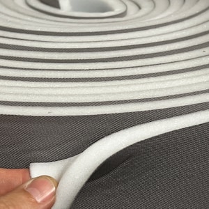 May include: A roll of white foam padding with a gray fabric backing. The foam is rolled up and the fabric is visible on the outside of the roll.