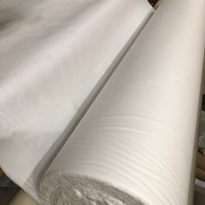 May include: A large roll of white fabric is being unrolled on a table. The fabric is smooth and has a slight sheen.