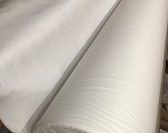 May include: A large roll of white fabric is being unrolled on a table. The fabric is smooth and has a slight sheen.