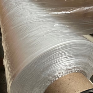 May include: A roll of clear plastic wrap on a cardboard core. The plastic wrap is tightly wound and has a slight sheen.