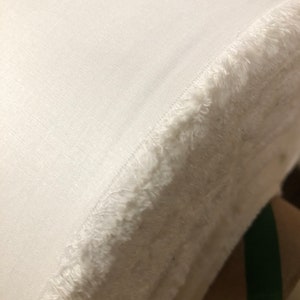 May include: A white fabric roll with a frayed edge. The fabric is smooth and has a slight sheen.