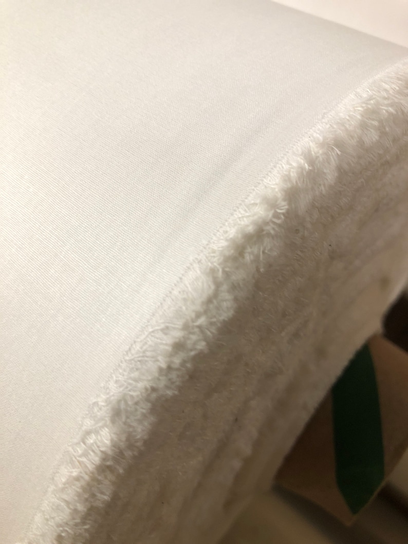 May include: A white fabric roll with a frayed edge. The fabric is smooth and has a slight sheen.