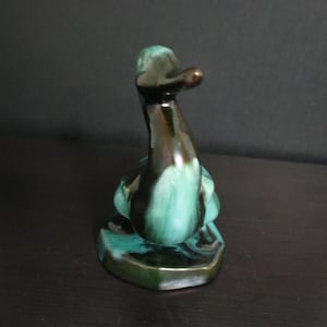 May include: A ceramic duck figurine in shades of green and brown. The duck has a glossy finish and is perched on a hexagonal base. The figurine is a decorative item.