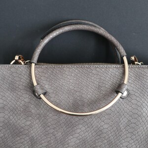 May include: Grey handbag with a snakeskin-effect texture. It has a gold-coloured, semi-circular handle and a matching zip. The handle is attached with gold-coloured hardware.