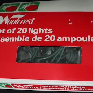 May include: A red and white box of Woolcrest Christmas lights. The box has a rectangular window showing green wires. The text on the box reads "Woolcrest set of 20 lights ensemble de 20 ampoules".