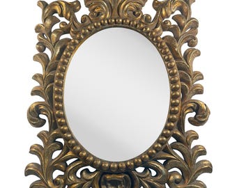 May include: Ornate gold-colored oval mirror with a decorative, scrolling frame. The frame features intricate leaf and floral designs, and a beaded border around the mirror's edge. The mirror is set against a white background.