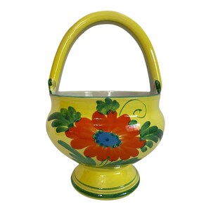 May include: A yellow ceramic basket with a handle, featuring a vibrant red and orange floral design with green leaves. The basket has a pedestal base and is suitable for decorative purposes.