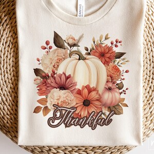 May include: A white t-shirt with a floral design featuring a pumpkin and the word "Thankful".