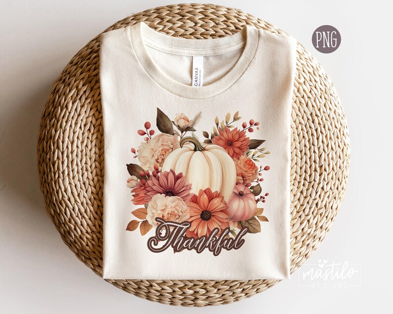 May include: A white t-shirt with a floral design featuring a pumpkin and the word "Thankful".