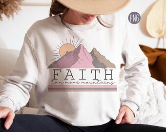 May include: A light gray crewneck sweatshirt featuring a graphic of a sun rising over mountains in shades of pink and brown. Below the mountains, the text reads FAITH Can move mountains, followed by three horizontal stripes in muted colors.