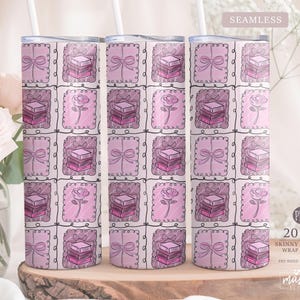 May include: Three 20 oz skinny tumblers with a repeating pattern of pink squares. Each square features a stack of books, a bow, or a rose. The tumblers have a seamless wrap design. The text "SEAMLESS" and "20 OZ SKINNY TUMBLER WRAP DESIGN" are visible.