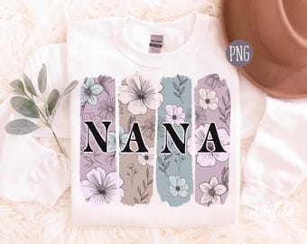 May include: A white crewneck sweatshirt featuring a graphic print of four vertical brushstroke panels in shades of lavender, beige, and sage green. Each panel contains black line-art floral illustrations and the black text NANA.