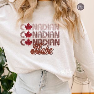 May include: A light gray sweatshirt with a red and white graphic design that says "Canadian Babe" with three maple leaf images.
