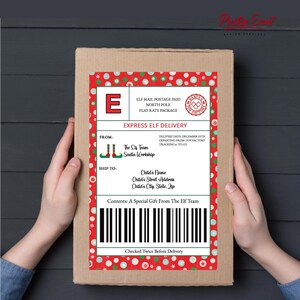 May include: A cardboard box with a red and white label featuring the text "Express Elf Delivery." The label includes the text "The Elf Team Santa Workshop" and a barcode. The box is held by two hands.