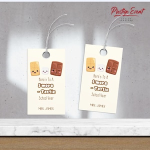 Puede incluir: Dos etiquetas de regalo blancas con un tema de s'more. Cada etiqueta presenta una galleta graham, un malvavisco y una barra de chocolate de dibujos animados con caras. El texto en las etiquetas dice "Here's to a S'more - Tastic School Year".