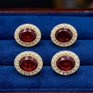 May include: Four oval red gemstone earrings with a gold border and a halo of small, clear gemstones. The earrings are presented in a blue velvet jewellery box with a wooden frame.