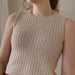 Op de afbeelding: Een mouwloos gebreid topje in een licht beige kleur. Het topje heeft een geribbelde textuur en een ronde hals.