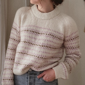Peut inclure: Un pull blanc à rayures roses et brunes. Le pull a un col rond et des manches longues.