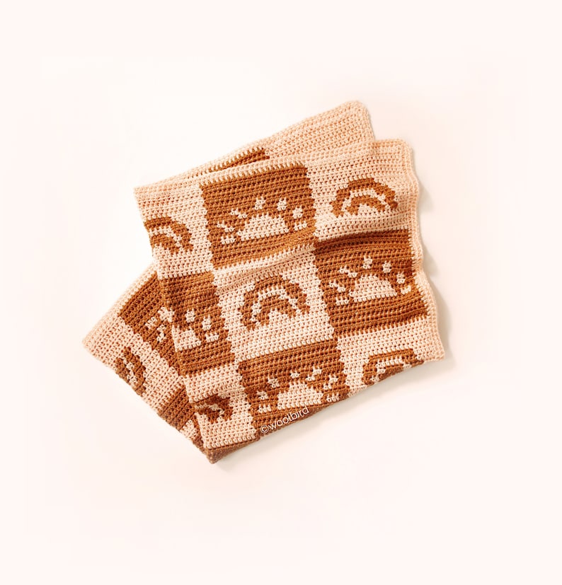 May include: A crocheted baby blanket with a brown and cream color scheme. The blanket features a repeating pattern of suns and rainbows.