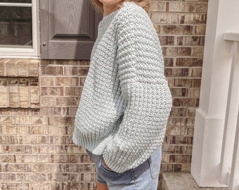 May include: A light blue knitted sweater with a loose fit and long sleeves. The sweater has a textured knit pattern.